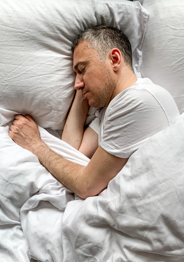 A middle aged man sleeping soundly on his side in a white bed
